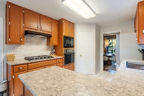 A kitchen with wooden cabinets, a gas stove, an oven, and a marble countertop. - Cowboy Cove Pool - Hot Tub - Arcade - Games (Austin)
