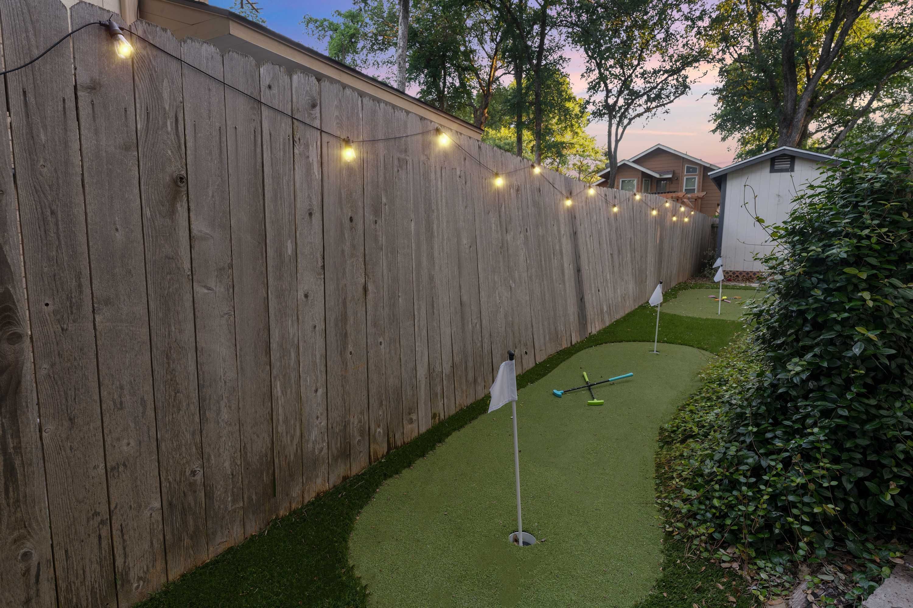 A backyard with a wooden fence, artificial grass, and a croquet set.