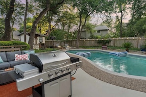 A backyard with a swimming pool, a barbecue grill, and a seating area with a sofa. - Cowboy Cove Pool - Hot Tub - Arcade - Games (Austin)
