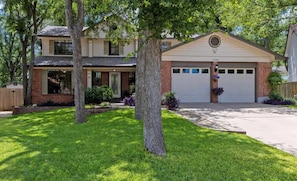A two-story house with a garage, surrounded by a well-maintained lawn and trees. - Cowboy Cove Pool - Hot Tub - Arcade - Games (Austin)