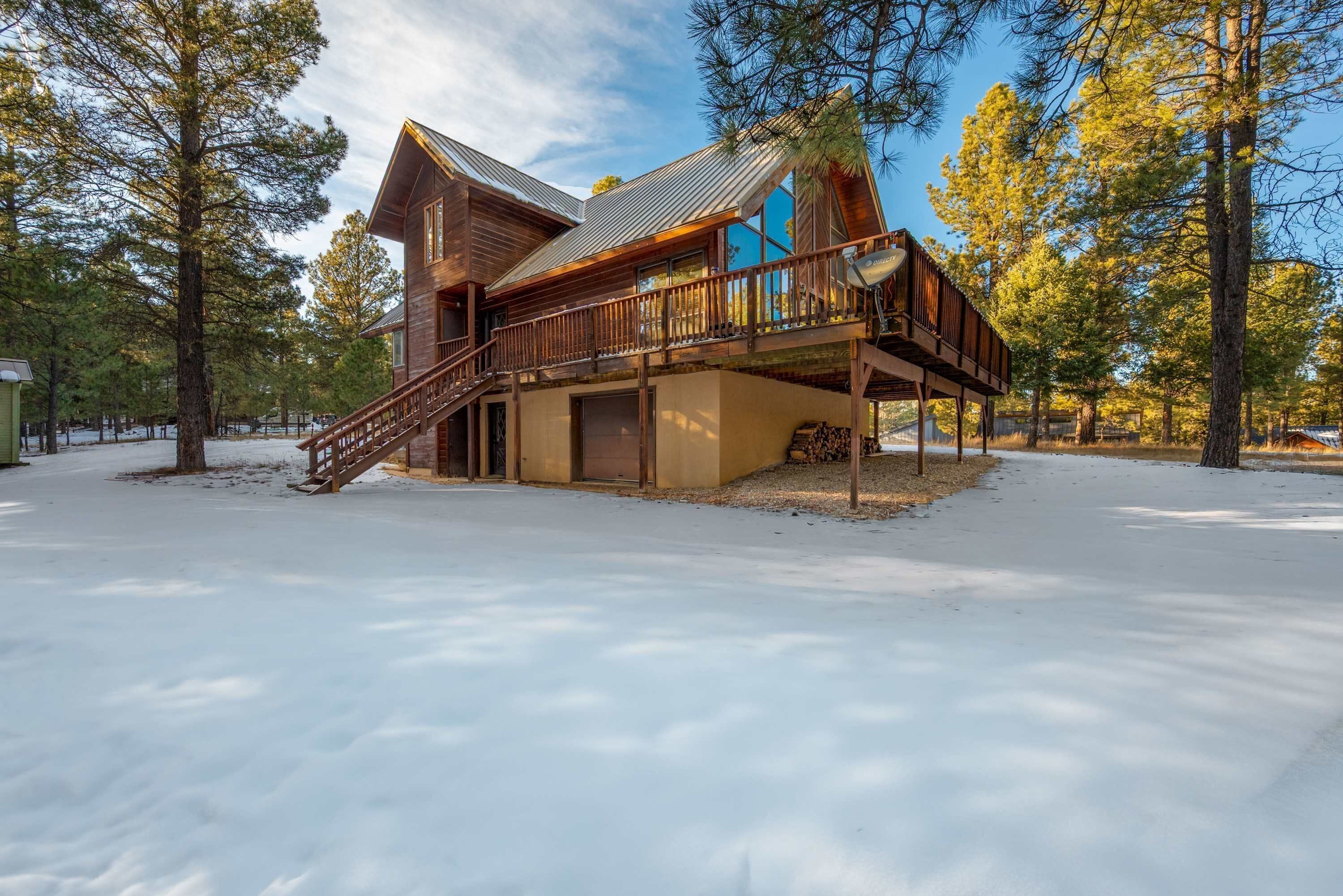 Una cabaña de madera con terraza y escaleras, rodeada de árboles y nieve.