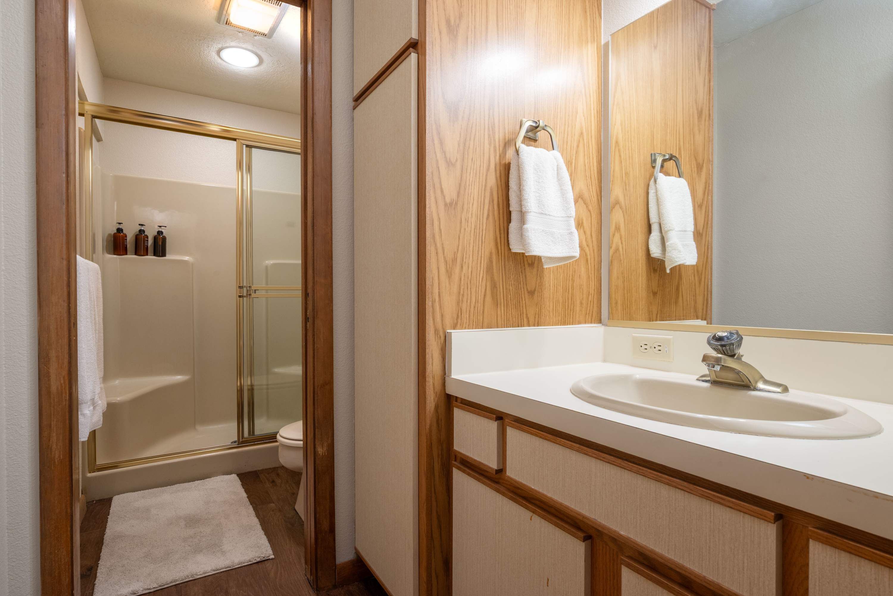 A bathroom with a glass shower enclosure, a sink with a mirror, and two towels hanging on hooks.