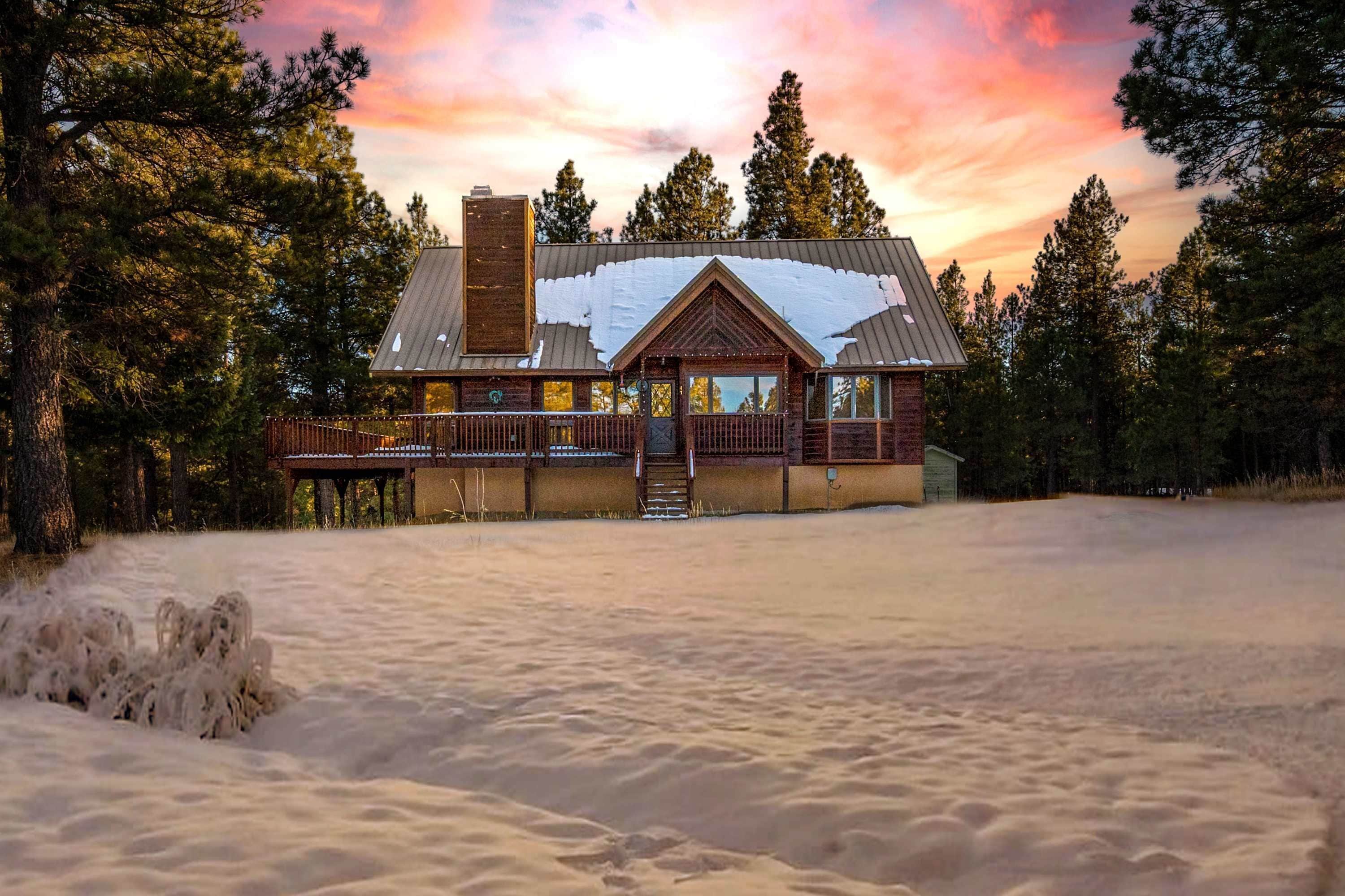 Una cabaña con una terraza amplia, rodeada de nieve y árboles, bajo un cielo al atardecer.