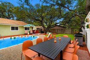 Un jardin avec une piscine, une table à manger avec des chaises et un patio couvert.