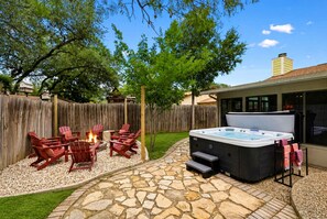 A backyard with a stone patio, outdoor seating, a hot tub, and a wooden fence. - Honky Tonk Dreams Pool - Hot Tub - Games (San Antonio)