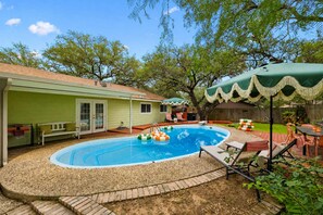 Ein Garten mit Schwimmbecken, einer überdachten Terrasse und einem eingezäunten Bereich.