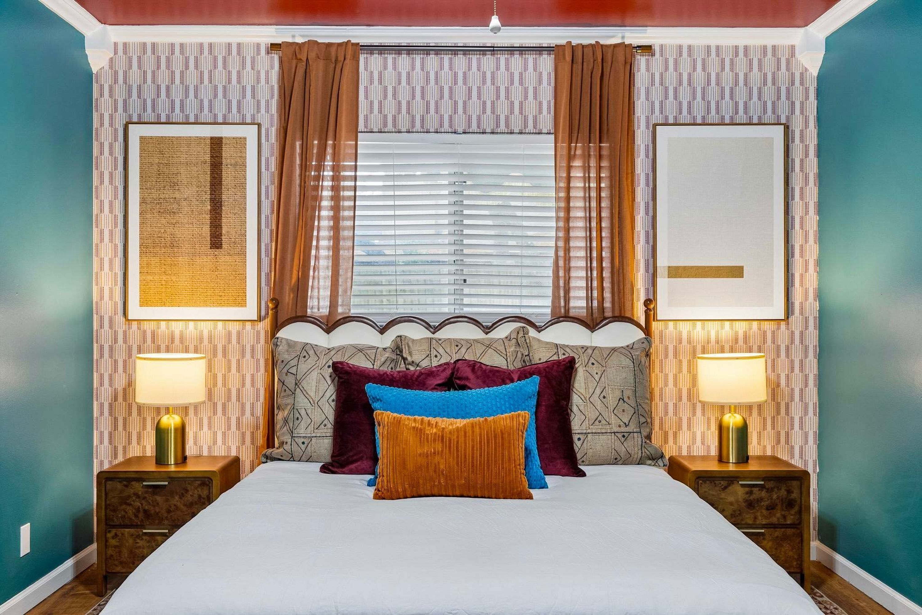 A bedroom with a bed, two bedside tables, a window with curtains, and two wall-mounted lamps.