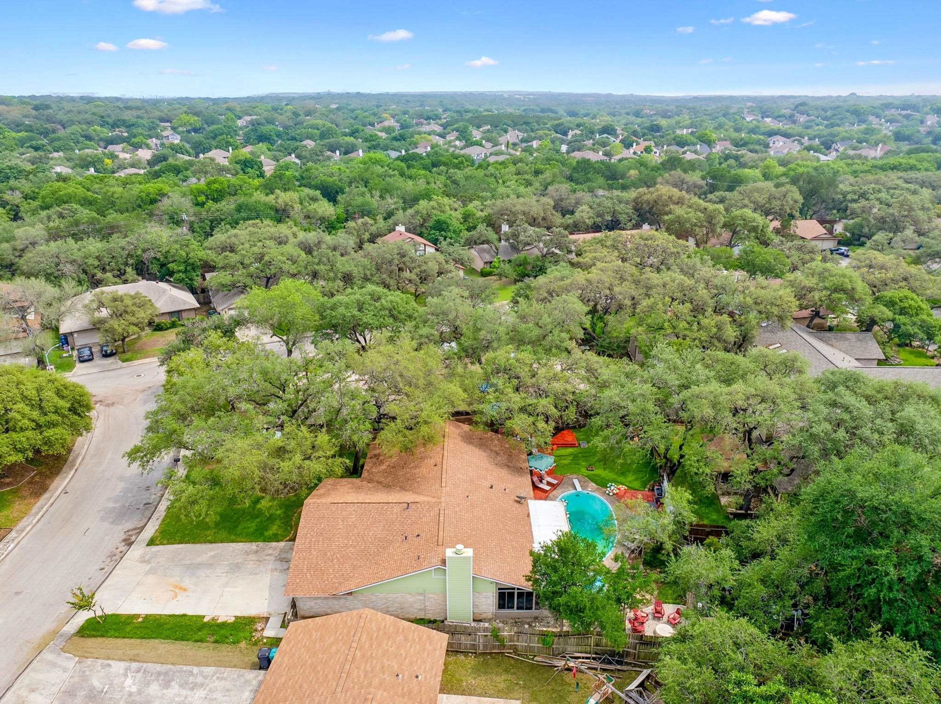 A residential area with houses surrounded by trees, a swimming pool, and a clear sky.