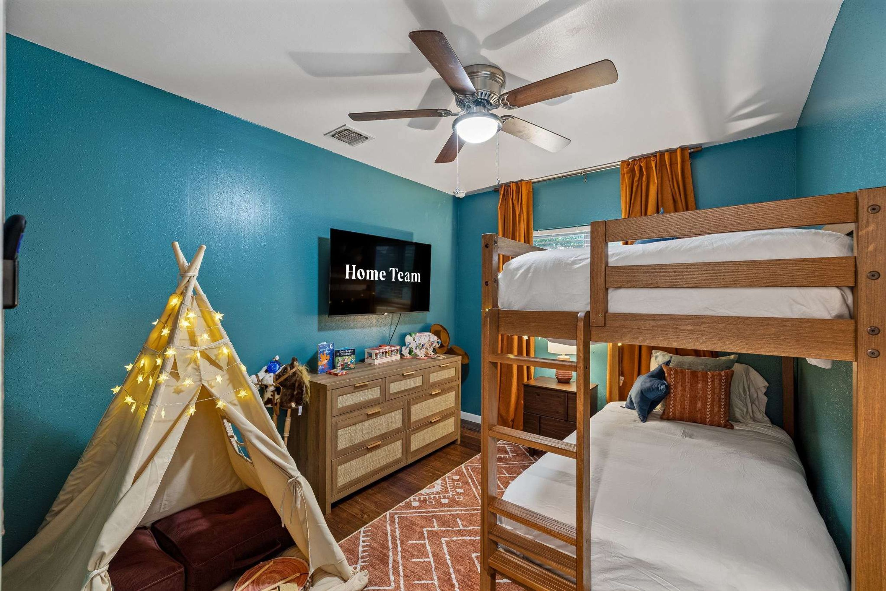A room with a bunk bed, a television, a ceiling fan, a tent, and a dresser.