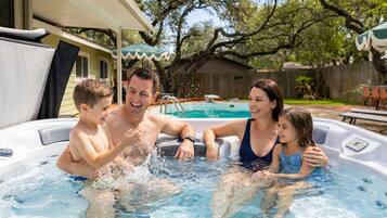 A family of four in a hot tub with a backyard setting.
