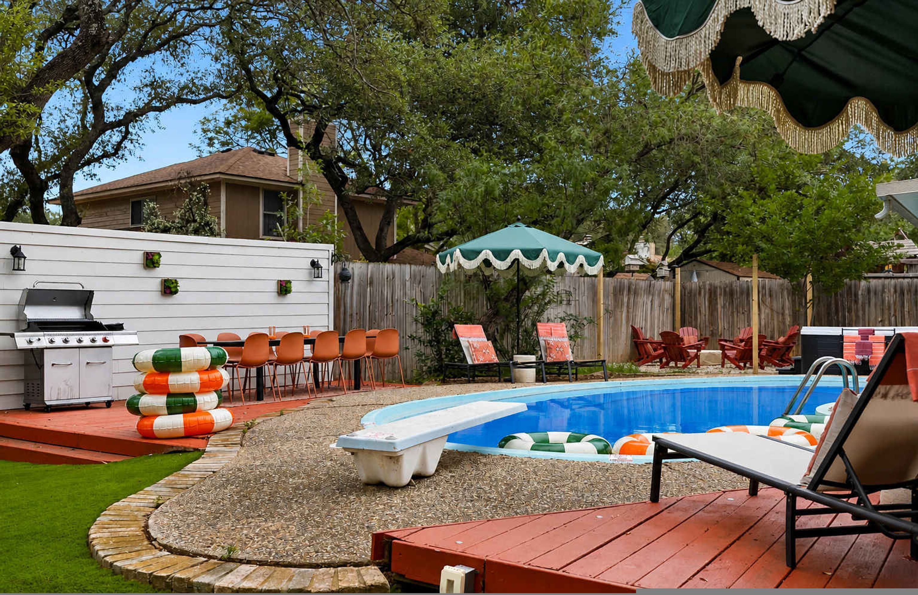 A backyard with a swimming pool, deck chairs, a barbecue grill, and a covered patio area.