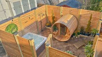 A wooden deck with a hot tub, a sauna, and potted plants.