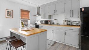 Una cocina moderna con armarios grises, encimera de madera, refrigerador negro y una ventana con persianas.