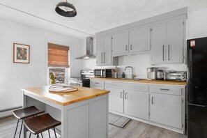 Una cocina moderna con armarios grises, encimera de madera, refrigerador negro y una ventana con persianas.