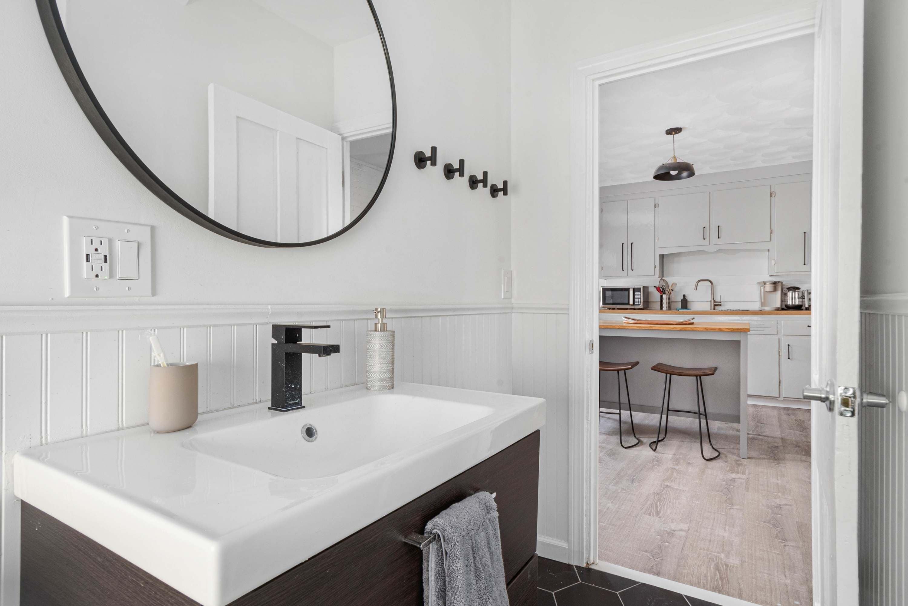 A modern bathroom with a large mirror, a white sink, and a dark wooden vanity.