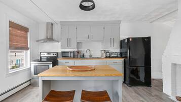 A modern kitchen with white cabinets, a black refrigerator, a wooden island with two stools, and a hanging light fixture.
