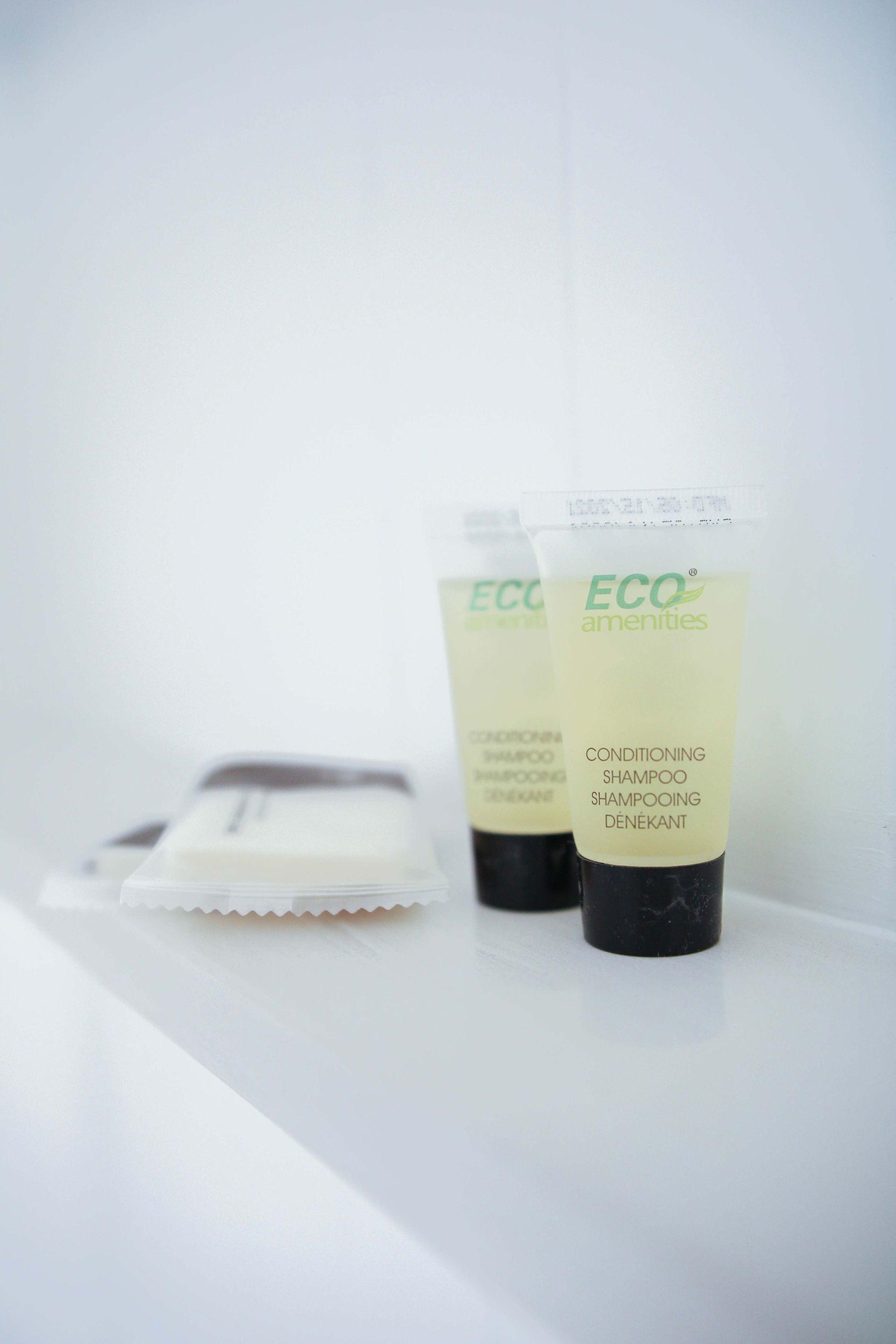 Two tubes of ECO amenities conditioning shampoo and a razor on a white surface.