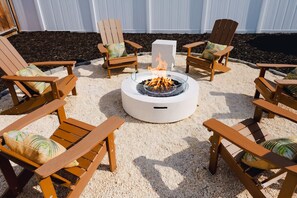 A circular fire pit surrounded by wooden Adirondack chairs with cushions, set on a gravel surface. - Sleeps 10 Outdoor Oasis Heated Pool Grill (Bradenton)