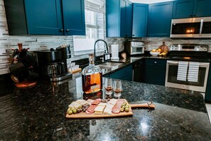 A kitchen with dark blue cabinets, a granite countertop, a coffee machine, a bottle of whiskey, glasses, and a charcuterie board with various meats and olives. - Sleeps 10 Outdoor Oasis Heated Pool Grill (Bradenton)