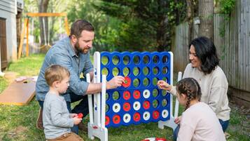 A family playing a board game outdoors with a wooden table and a grassy yard in the background.