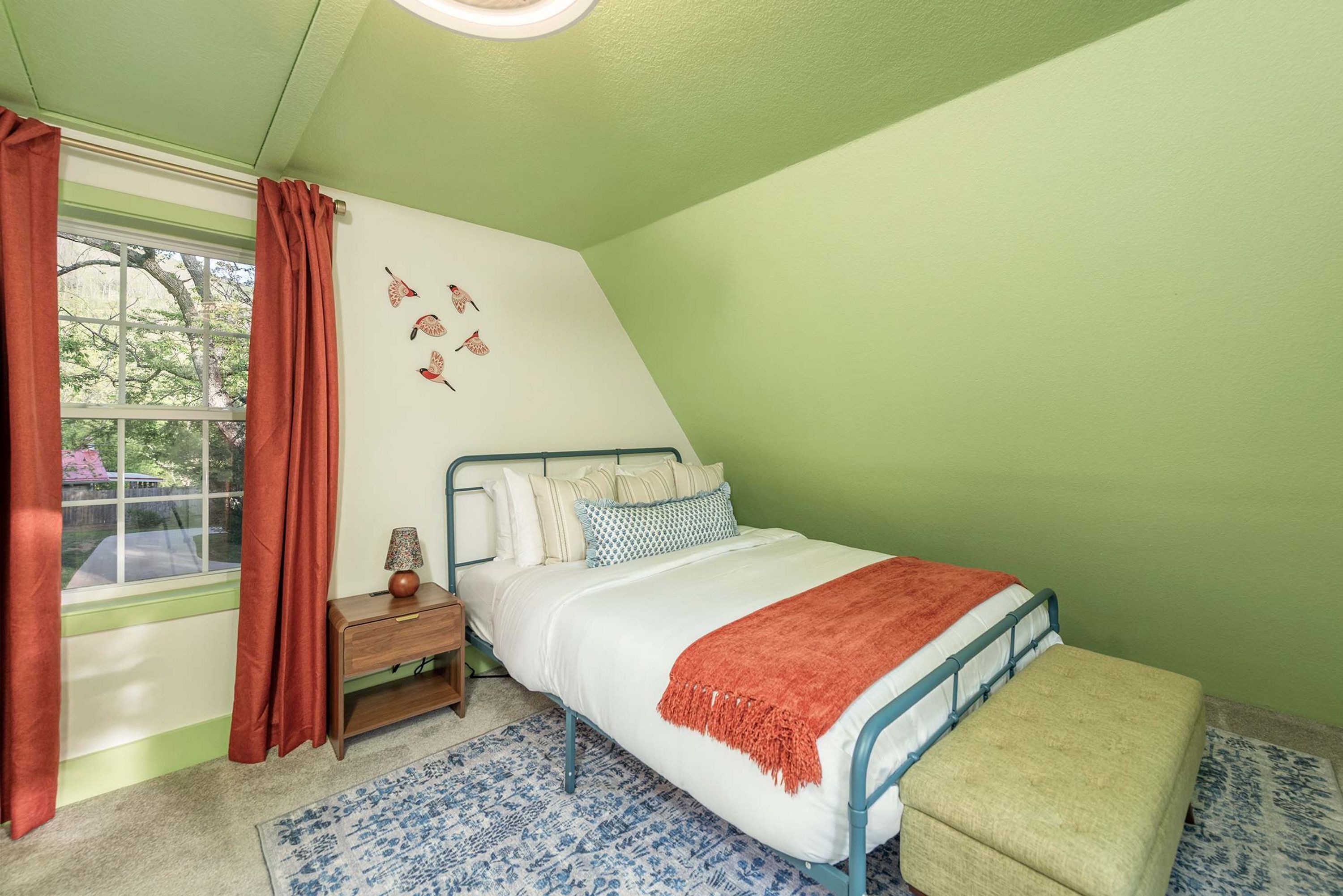 A bedroom with a bed, a nightstand, a lamp, a window with curtains, and a wall with bird decals.