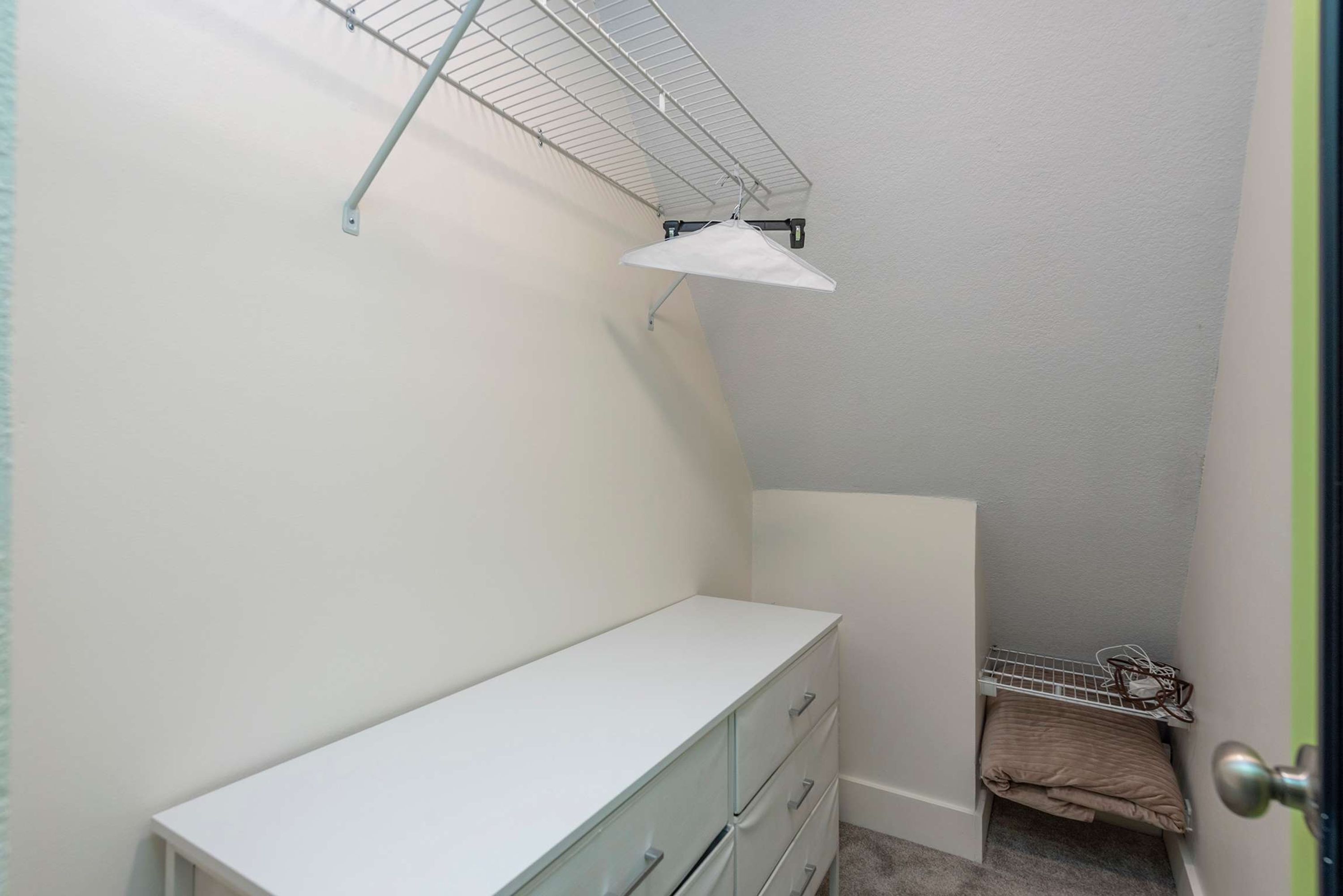 A small, enclosed room with a white dresser, a metal shelf, and a door with a round handle.