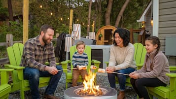 A family of four sitting on green chairs around a round outdoor fire pit.