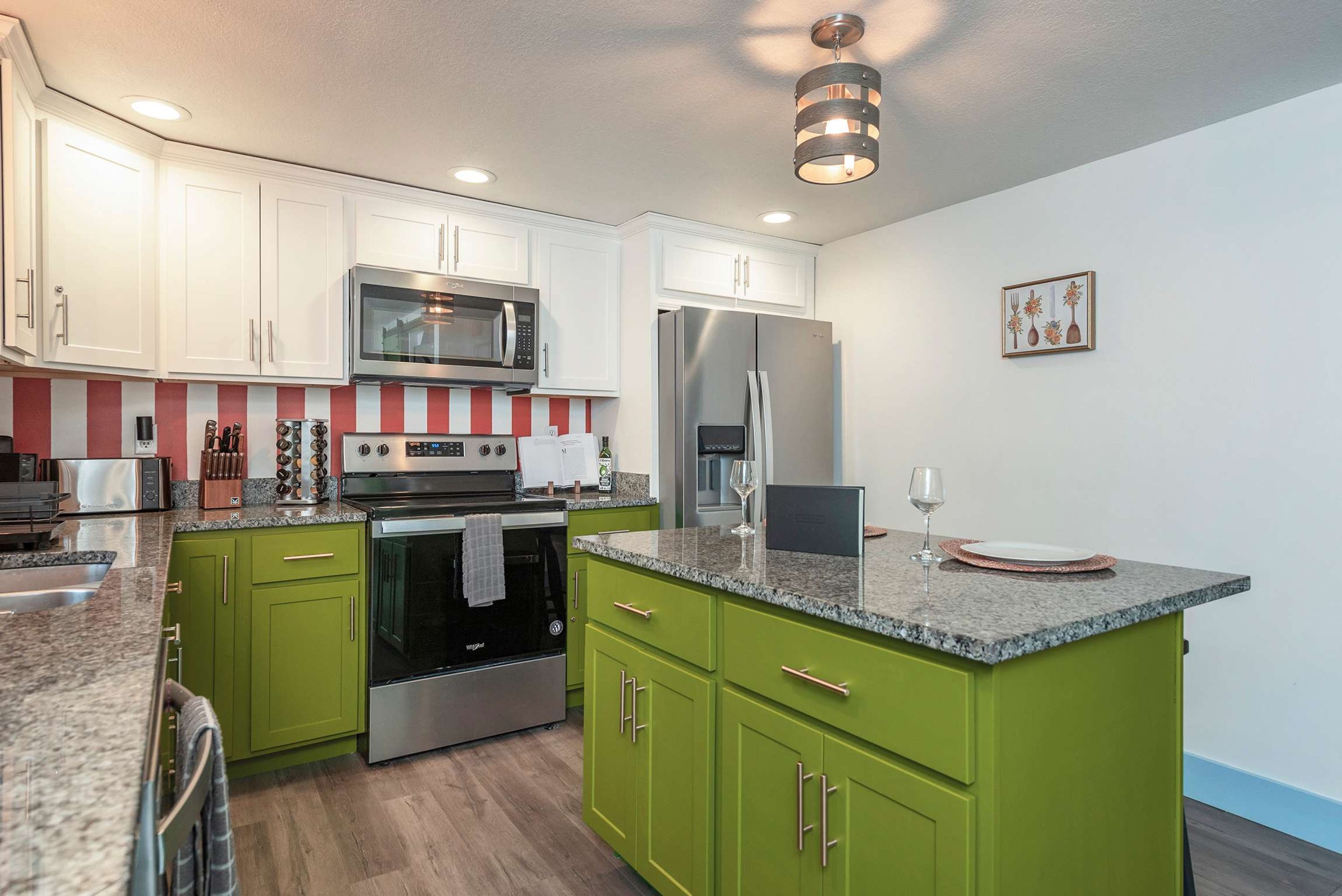 A modern kitchen with green cabinets, stainless steel appliances, and a red and white striped backsplash.