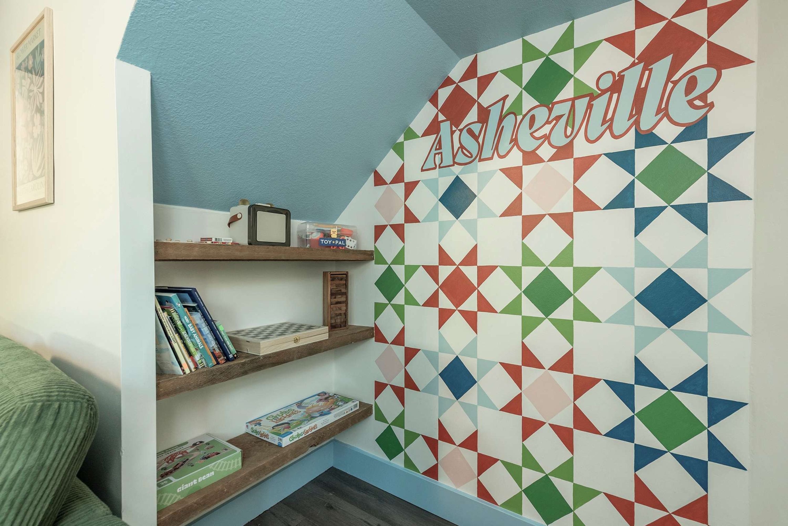Una habitación con un papel tapiz de diseño geométrico, estantes con libros y juguetes, y un cuadro en la pared.