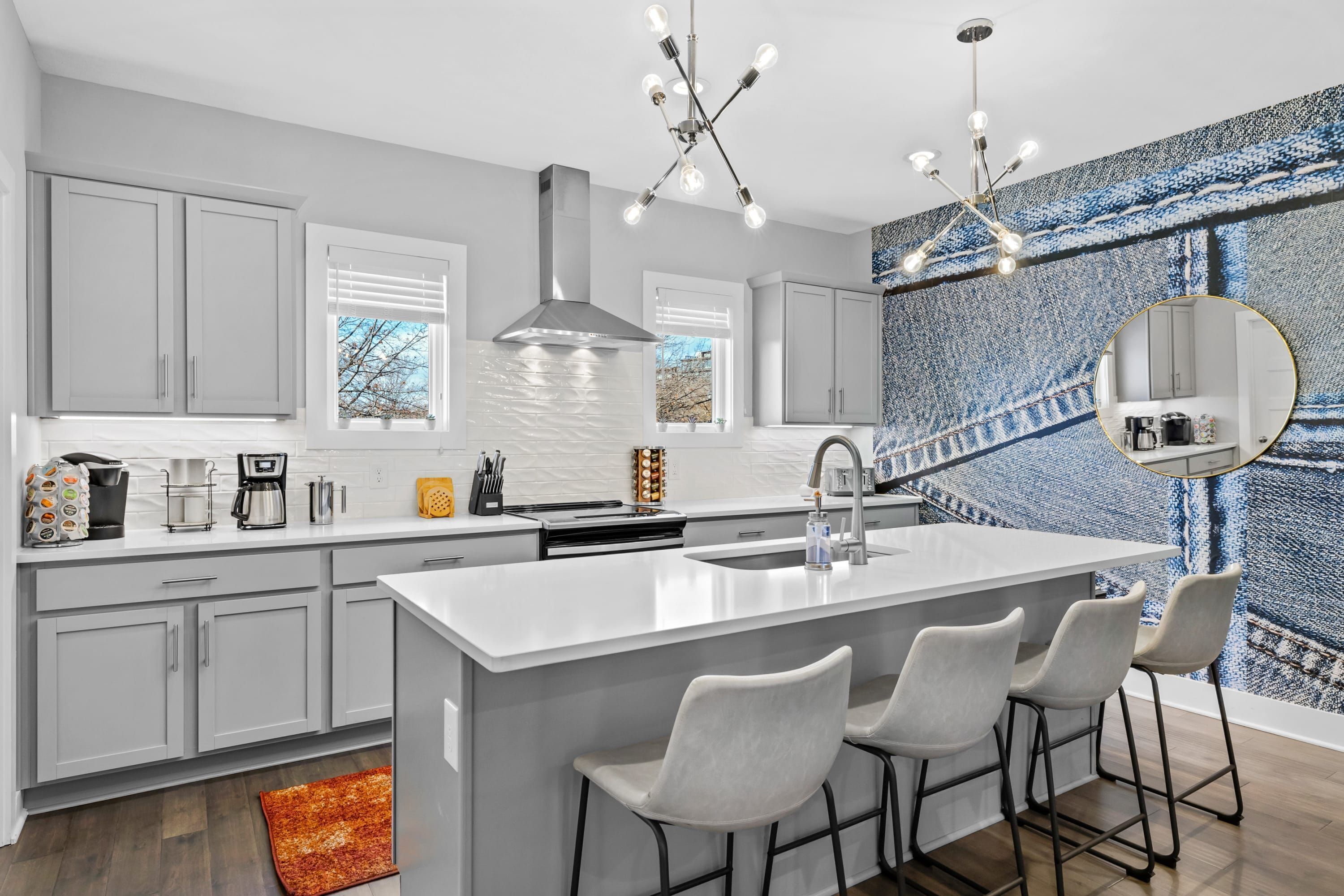 A modern kitchen with a central island, bar stools, a large window, and a patterned wall.