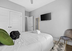 Quarto com cama, televisão de tela plana, espelho e cadeira.
