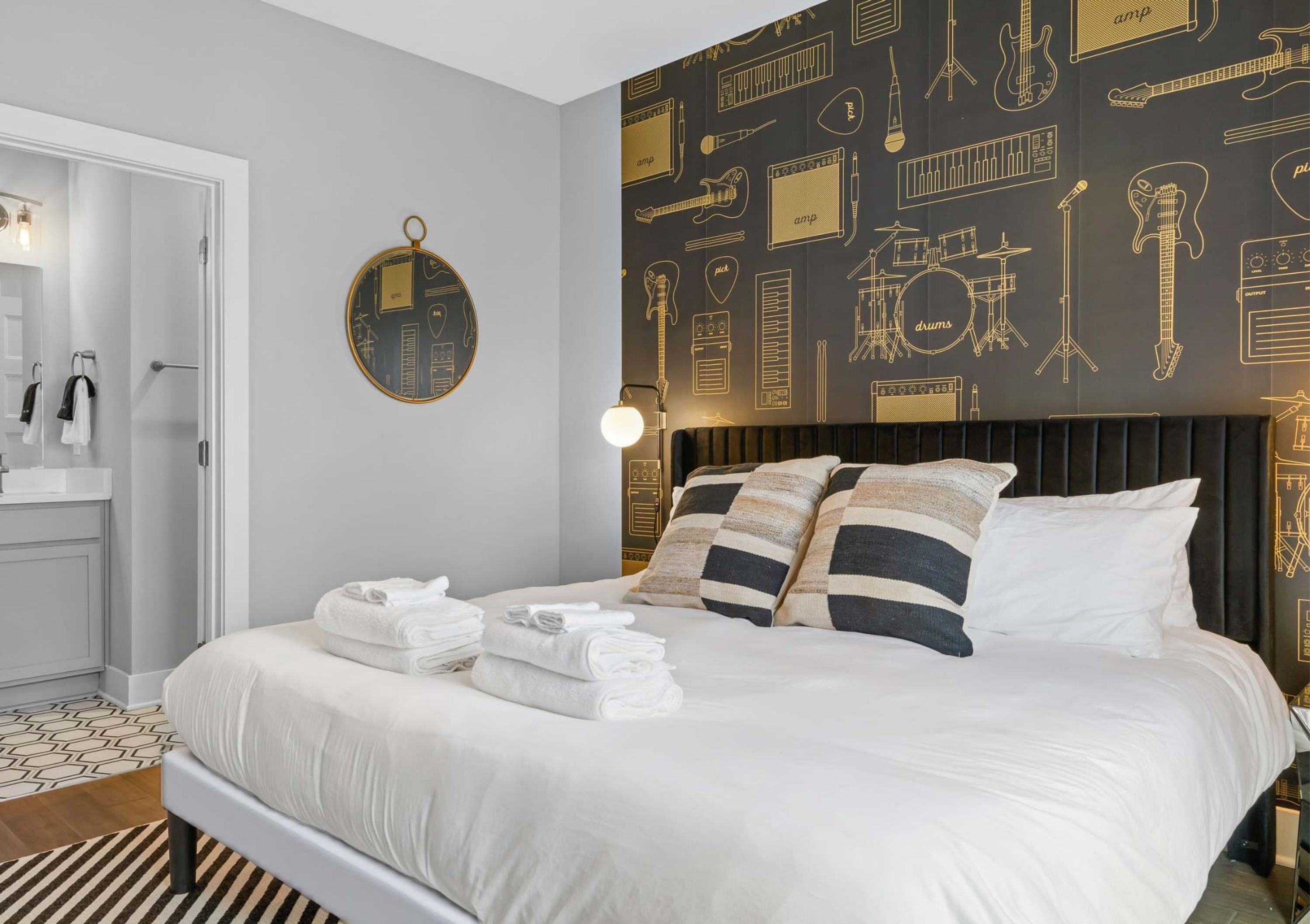 Une chambre d’hôtel avec un lit, des oreillers, un miroir rond et un mur décoré de motifs représentant des instruments de musique.