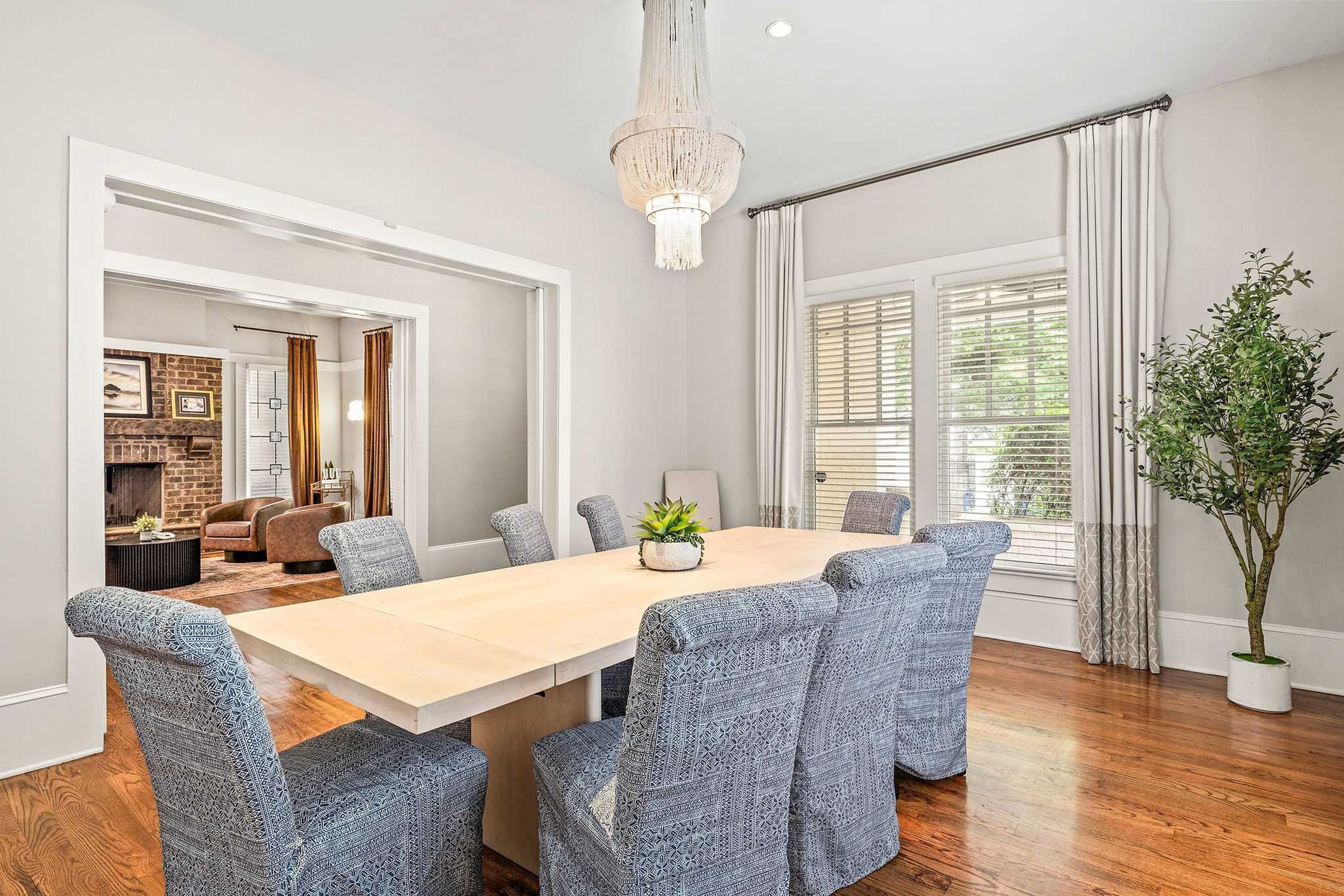 A dining room with a wooden table and patterned chairs, a chandelier, and a view of a living area with a fireplace.