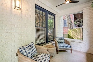 A room with a white brick wall, a large window with blinds, wicker furniture, and a ceiling fan. - Atlanta Beltline House City Center (Atlanta)