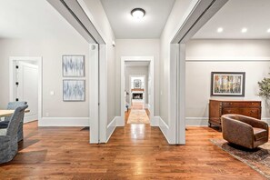 A hallway with hardwood flooring, white walls, and a fireplace in the distance. There are framed artworks on the walls and a brown leather armchair. - Atlanta Beltline House City Center (Atlanta)