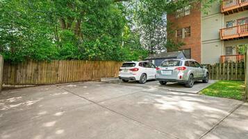 A residential driveway with two cars parked, a wooden fence, and a building with a balcony.