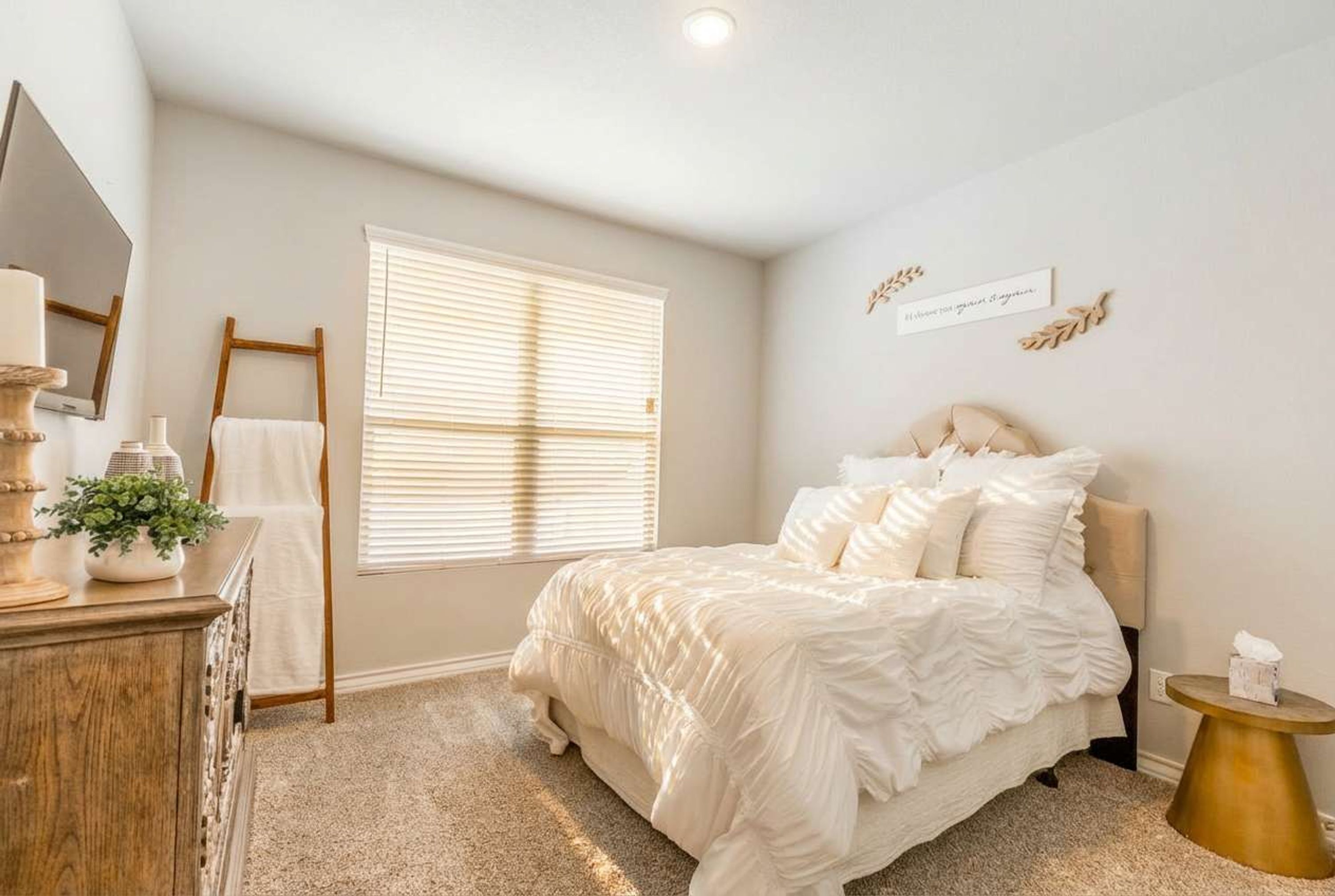 A bedroom with a bed, a dresser, a window with blinds, a mirror, and a bedside table.