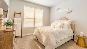 A bedroom with a bed, a dresser, a window with blinds, a mirror, and a bedside table. - 10 Minutes to Stadium Spacious 3BR Gameroom (Lubbock)