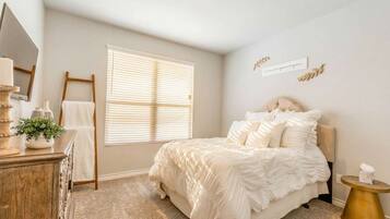 A bedroom with a bed, a dresser, a window with blinds, a mirror, and a bedside table.