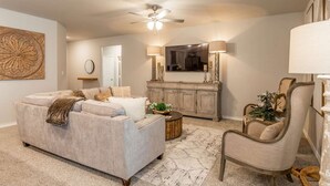 A living room with a sofa, a chair, a television, and a ceiling fan. - 10 Minutes to Stadium Spacious 3BR Gameroom (Lubbock)