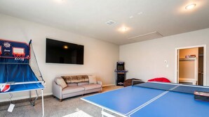 A room with a ping pong table, a sofa, a TV, and a basketball arcade. - 10 Minutes to Stadium Spacious 3BR Gameroom (Lubbock)