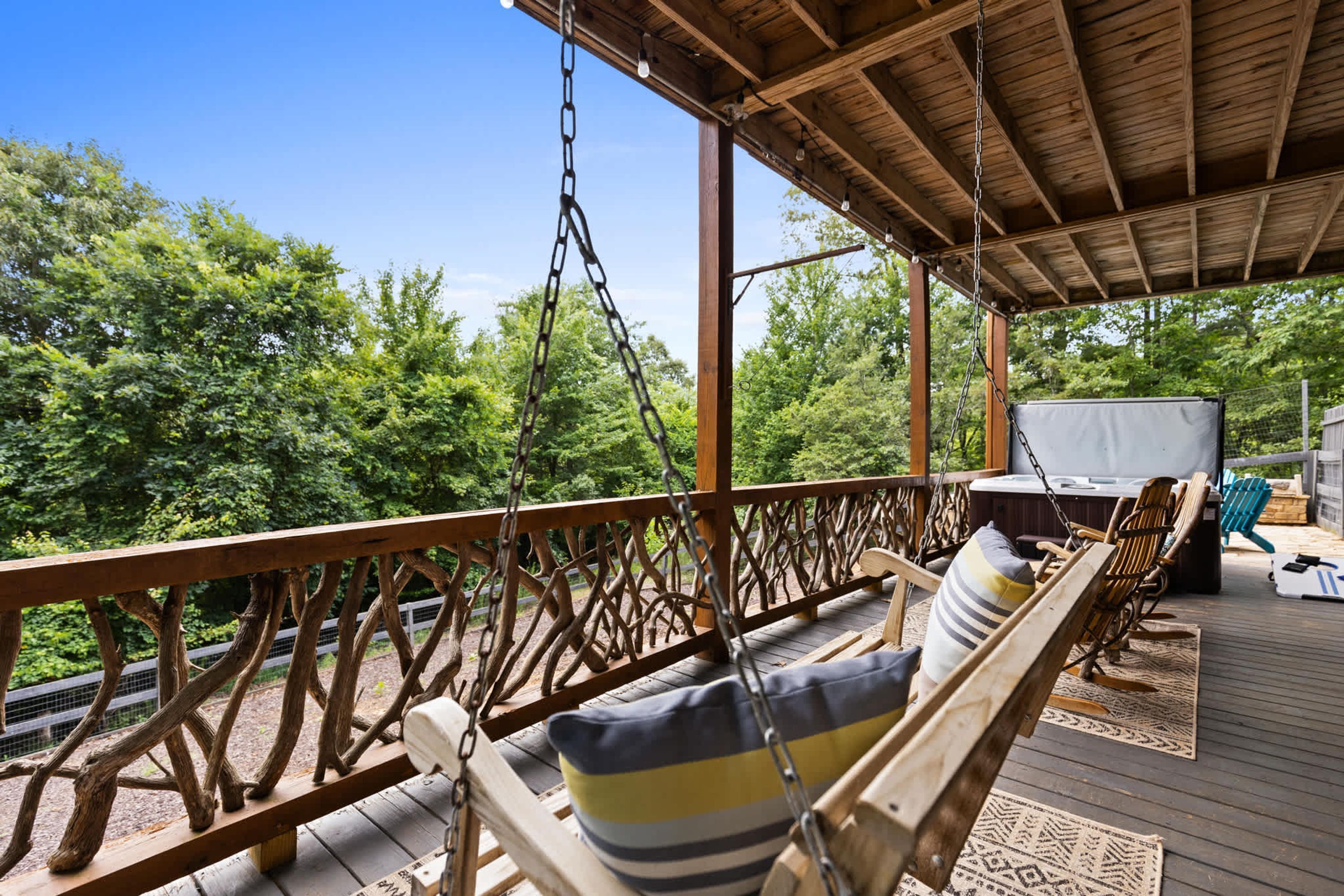 Un espace extérieur aménagé avec des bancs en bois et des coussins, un barbecue et une vue sur les arbres.