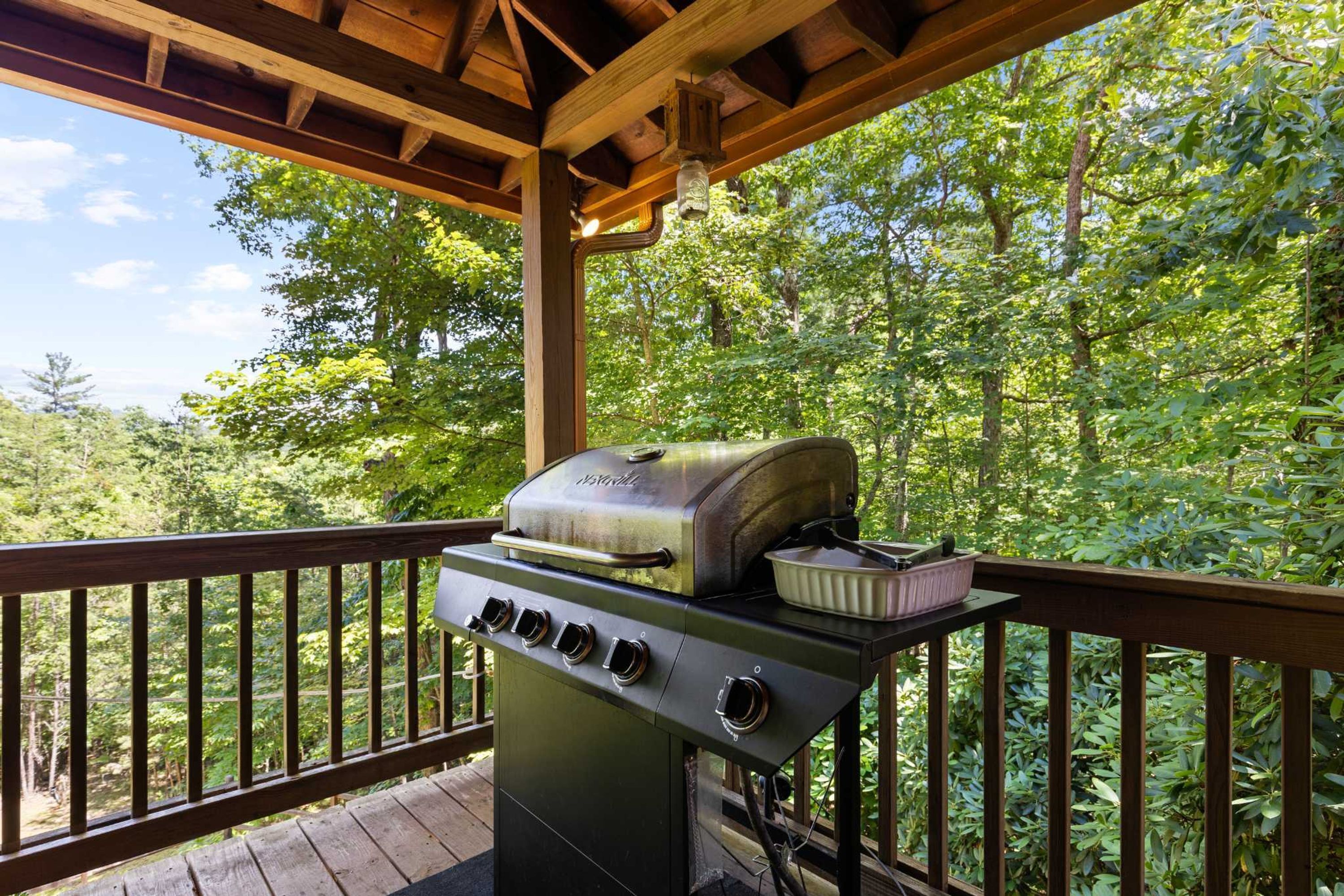 A barbecue grill on an outdoor deck with a view of a forested area.