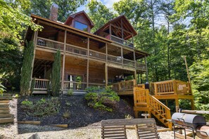 A two-story log cabin with a balcony, surrounded by a forest.