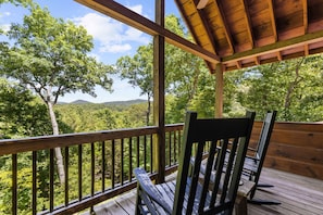 Um deck de madeira com vista para uma floresta e colinas.