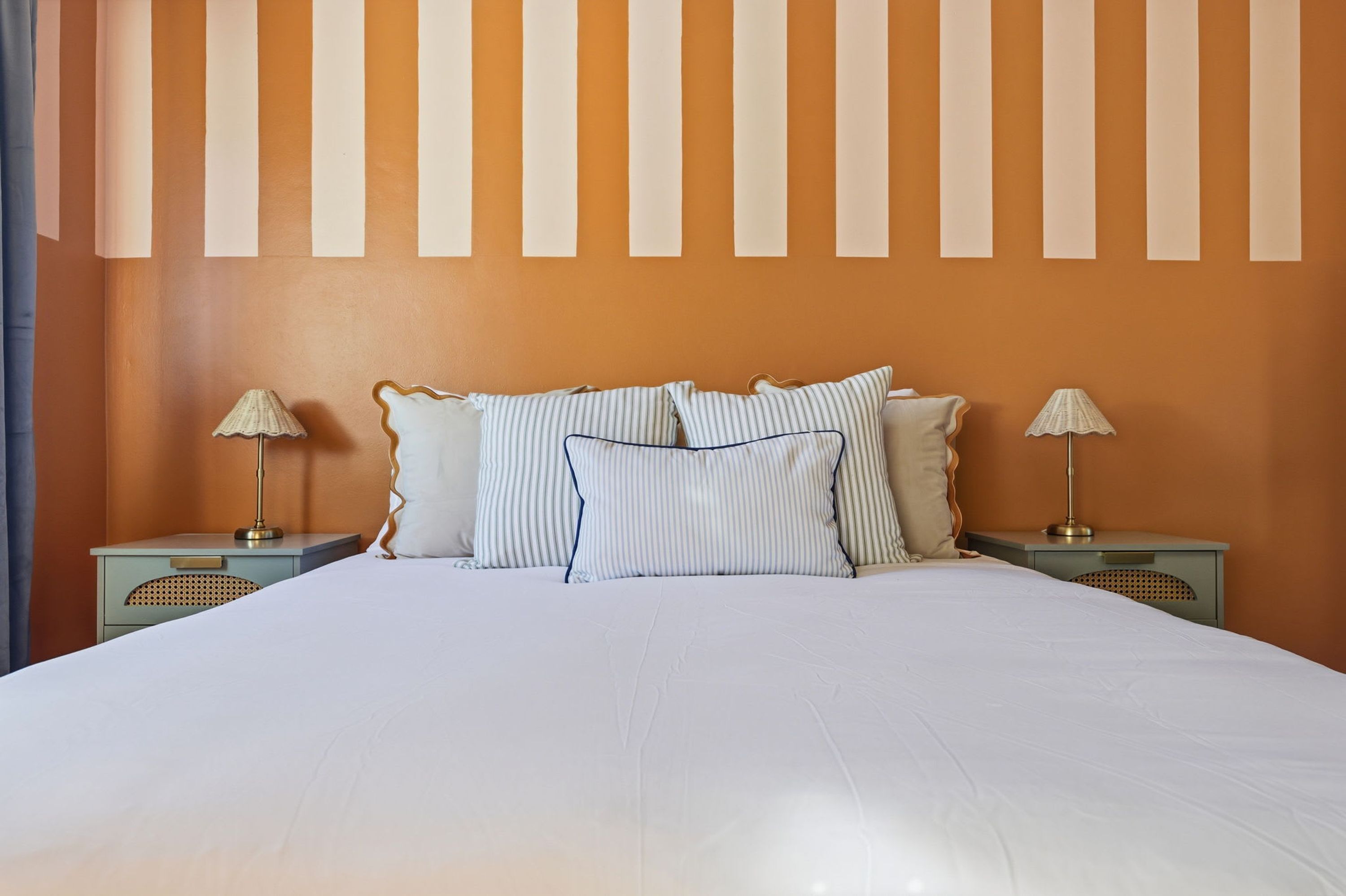 A hotel room with a large bed, two bedside tables with lamps, and a wall with vertical stripes.