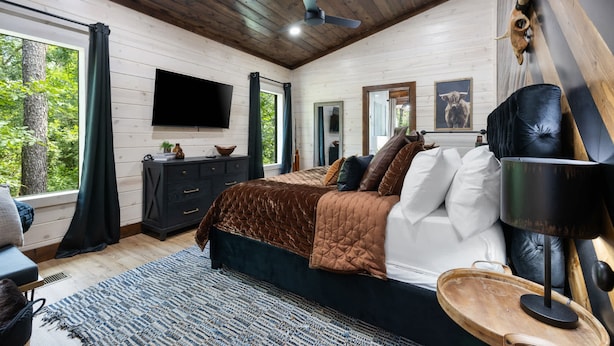 A bedroom with a bed, a TV, a dresser, a mirror, and a ceiling fan. - Broken Bow Luxury Cabin Hot Tub Playset Games (Broken Bow)