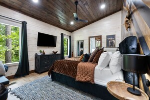 Un dormitorio con cama, televisor, cómoda, espejo y ventilador de techo.