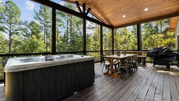 A wooden deck with a hot tub, outdoor seating, and a view of trees.