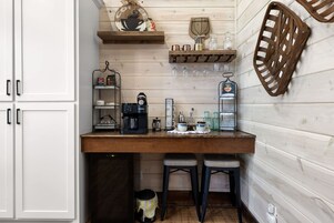 Cocina con mostrador de madera, cafetera y taburetes de bar.